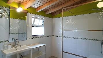 Ein Badezimmer mit Holzboden, einem weißen Waschbecken mit Spiegel, einer Duschkabine und einem Fenster.