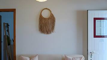 Une pièce chaleureuse avec un plafond en bois, une décoration murale en macramé suspendue, un canapé blanc agrémenté de deux coussins et une porte avec une pancarte.
