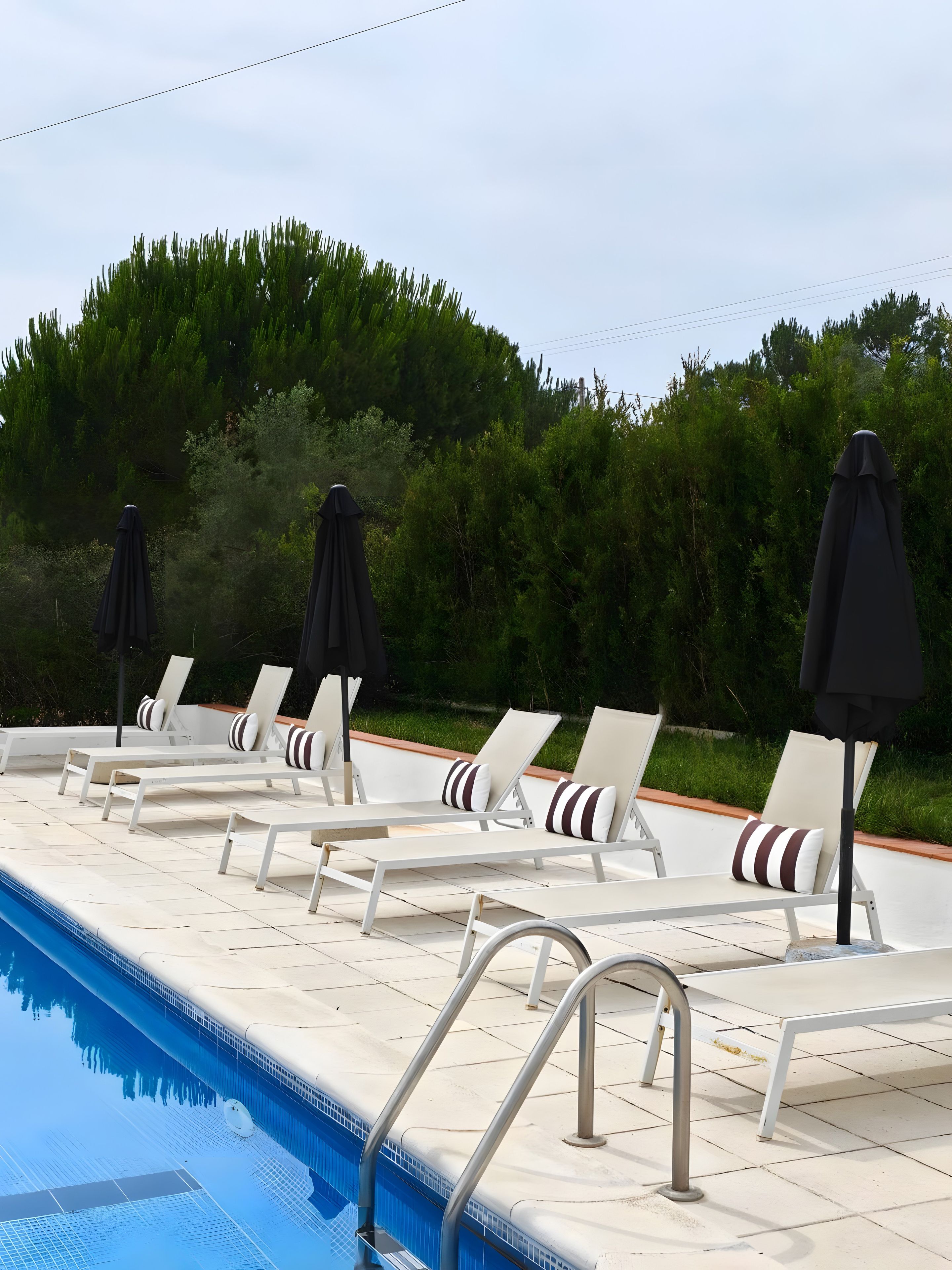 A poolside area with lounge chairs and umbrellas, surrounded by greenery.