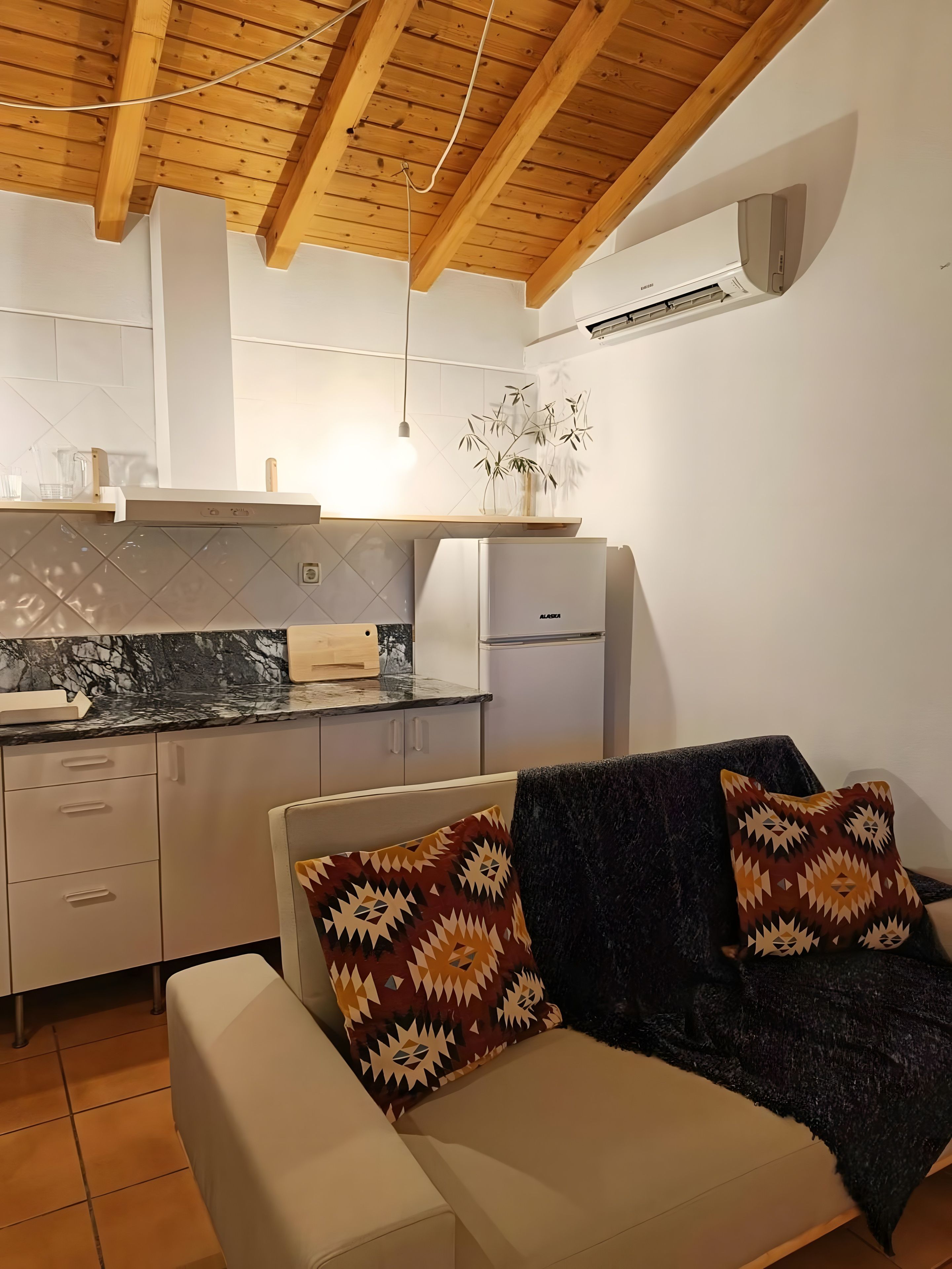 A modern kitchen with a built-in stove, a refrigerator, and a dining area with a sofa and cushions.