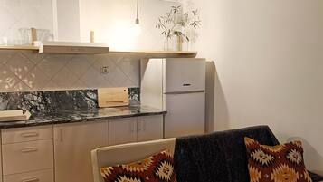 A modern kitchen with a built-in stove, a refrigerator, and a dining area with a sofa and cushions.