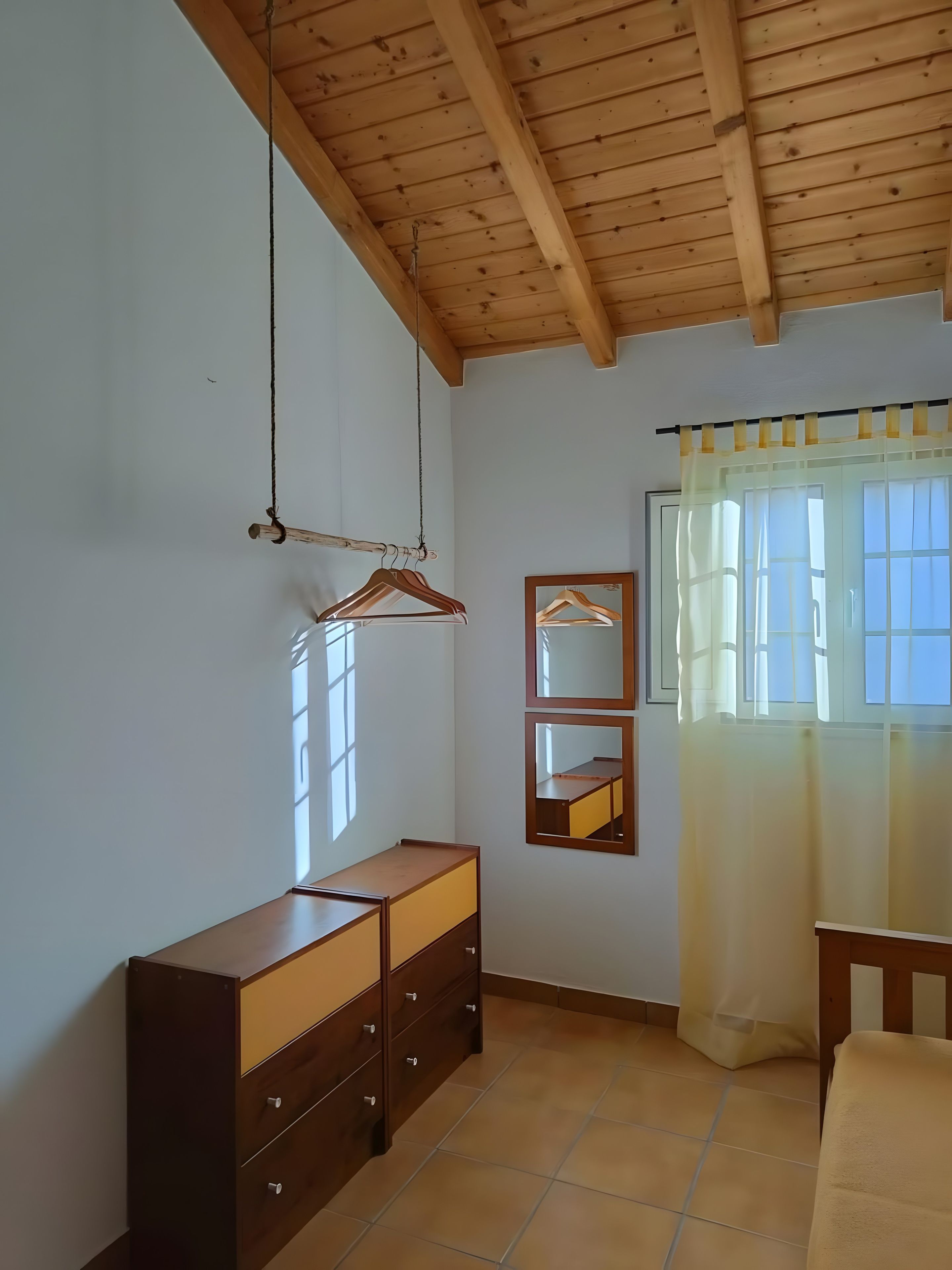 Una habitación con techo y aparador de madera, un espejo y una ventana con cortinas.