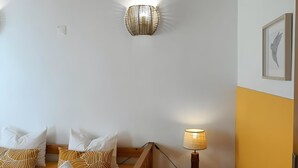 A bedroom with a wooden bed, white and patterned pillows, a wall-mounted light fixture, a bedside table with a lamp, and a framed picture on the wall. - Apartment 'Casa Medronheiro' with Mountain View, Wi-Fi and Air Conditioning (Melides)