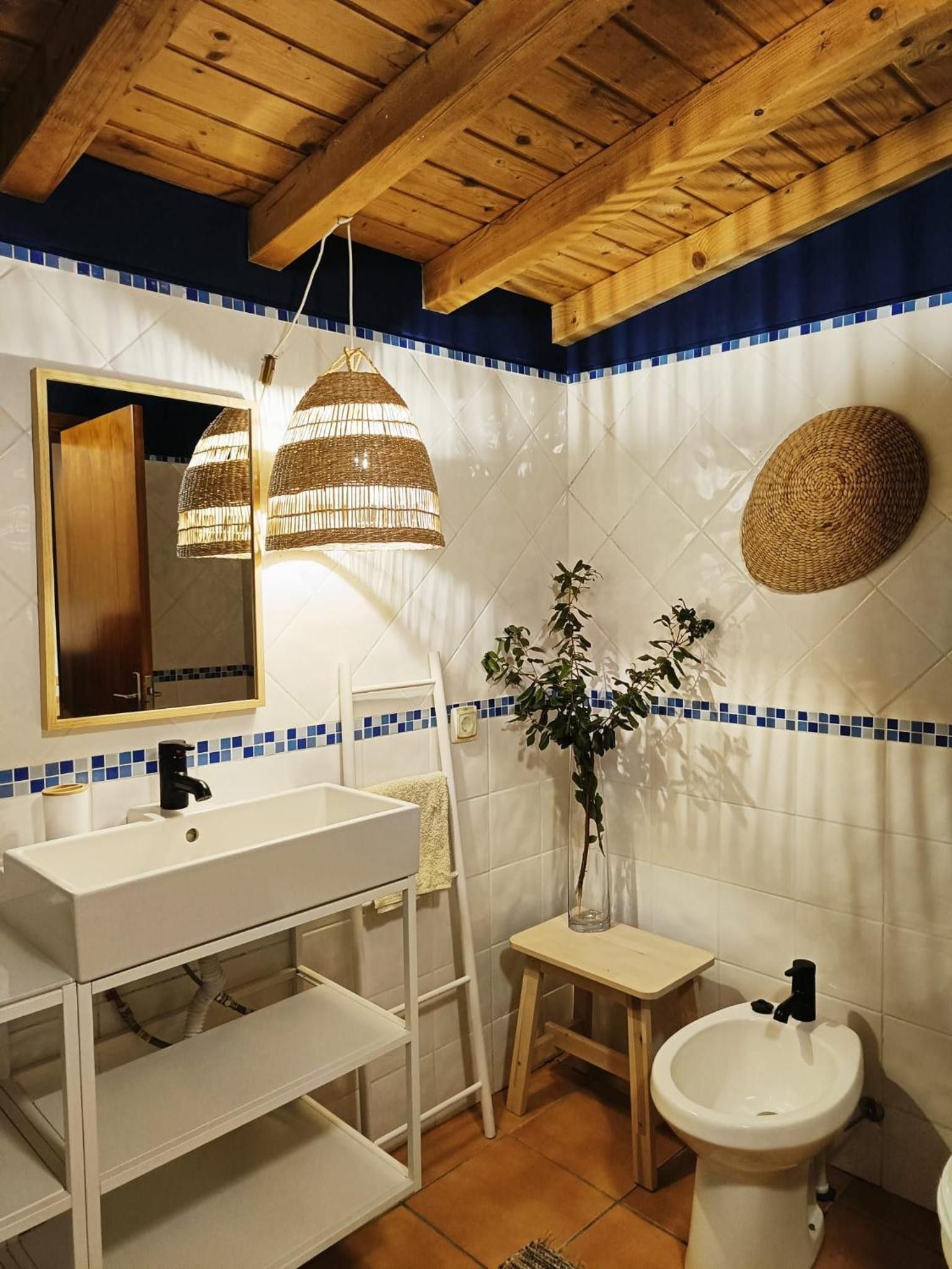 A bathroom with a wooden ceiling, a white sink, a mirror, and a blue-tiled wall.