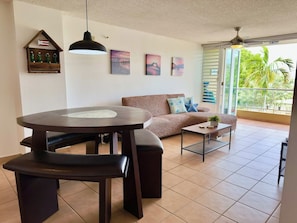 Un salon avec une table ronde, un canapé et un balcon offrant une vue sur les palmiers.