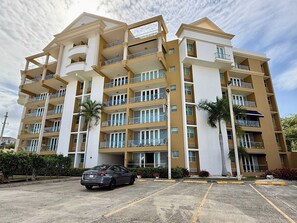 A multi-story residential building with balconies, a parking lot, and palm trees. - Family-Friendly | Year-Round Pool & Beach Nearby (Boquerón)