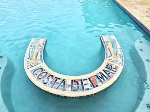 Une piscine dont le bord est décoré d’une mosaïque formant l’inscription « COSTA DEL MAR ».