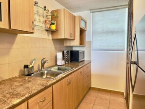 A kitchen with a granite countertop, stainless steel sink, wooden cabinets, a microwave, and a refrigerator. - Family-Friendly | Year-Round Pool & Beach Nearby (Boquerón)
