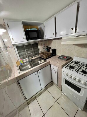 A compact kitchen with a stove, sink, and cabinets. - Near Beach Stay | Pool Access, Tennis & Games (Boquerón)