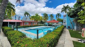 A swimming pool surrounded by greenery, with buildings in the background. - Near Beach Stay | Pool Access, Tennis & Games (Boquerón)