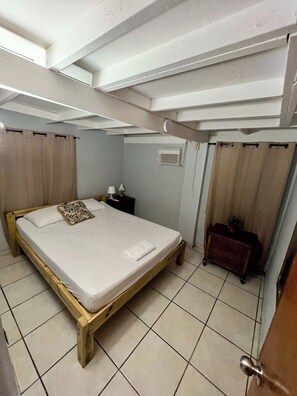 A room with a wooden bed, a nightstand, a small cabinet, and a window with curtains. - Near Beach Stay | Pool Access, Tennis & Games (Boquerón)