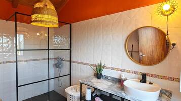 Un baño con cabina de ducha de vidrio, un lavamanos blanco sobre encimera de mármol y techo de madera.