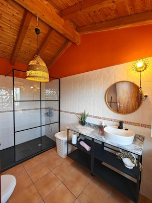 Een badkamer met een douchecabine van glas, een wit wastafelmeubel met een marmeren blad en een houten plafond.
