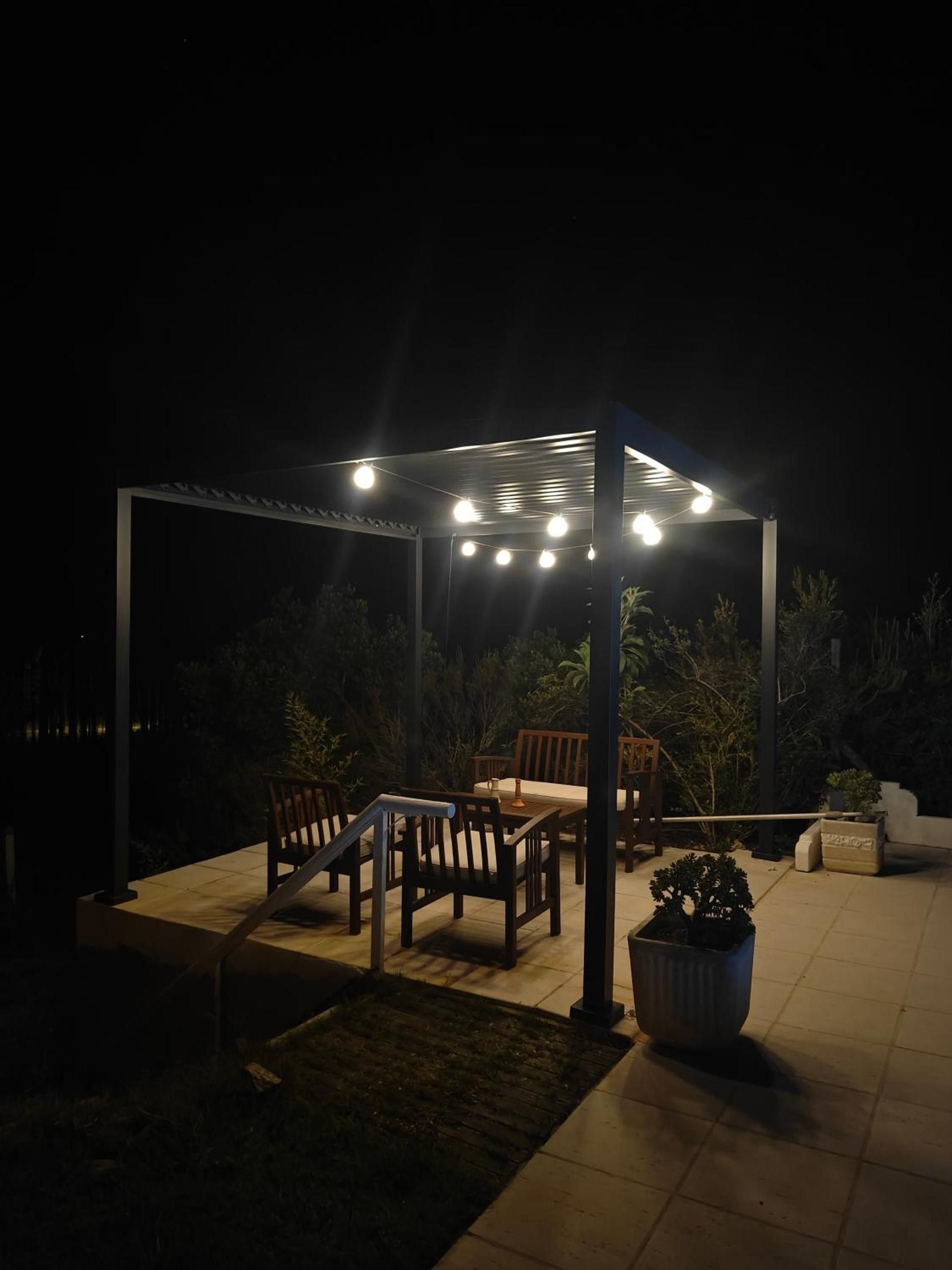 An outdoor patio area with a pergola, seating, and potted plants.
