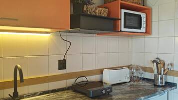 Uma cozinha com pia, micro-ondas, torradeira e bancada com torradeira e copos.