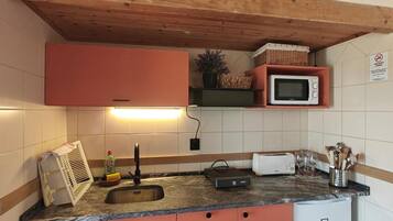 Una cocina con microondas incorporado, un lavamanos y un refrigerador pequeño.