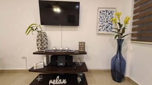 Un salon moderne avec un téléviseur à écran plat fixé au mur, une console décorative avec des haut-parleurs et un vase bleu contenant des fleurs jaunes.