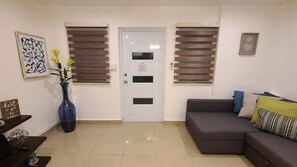 A living room with a grey sofa, a vase with flowers, and a door with a window. - Family-Friendly Condo Near Beach and Nightlife (Boquerón)