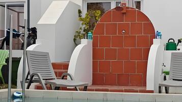 Ein Poolbereich mit Liegestühlen, einem Grill und einer Ziegelwand.