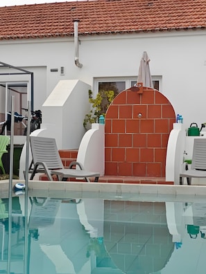 A pool area with lounge chairs, a barbecue grill, and a brick wall. - Apartment 'Casinha De Lume' with Mountain View, Wi-Fi and Air Conditioning (Melides)