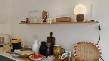 Una cocina con encimera blanca, diversos alimentos, una cafetera y una lámpara colgante.
