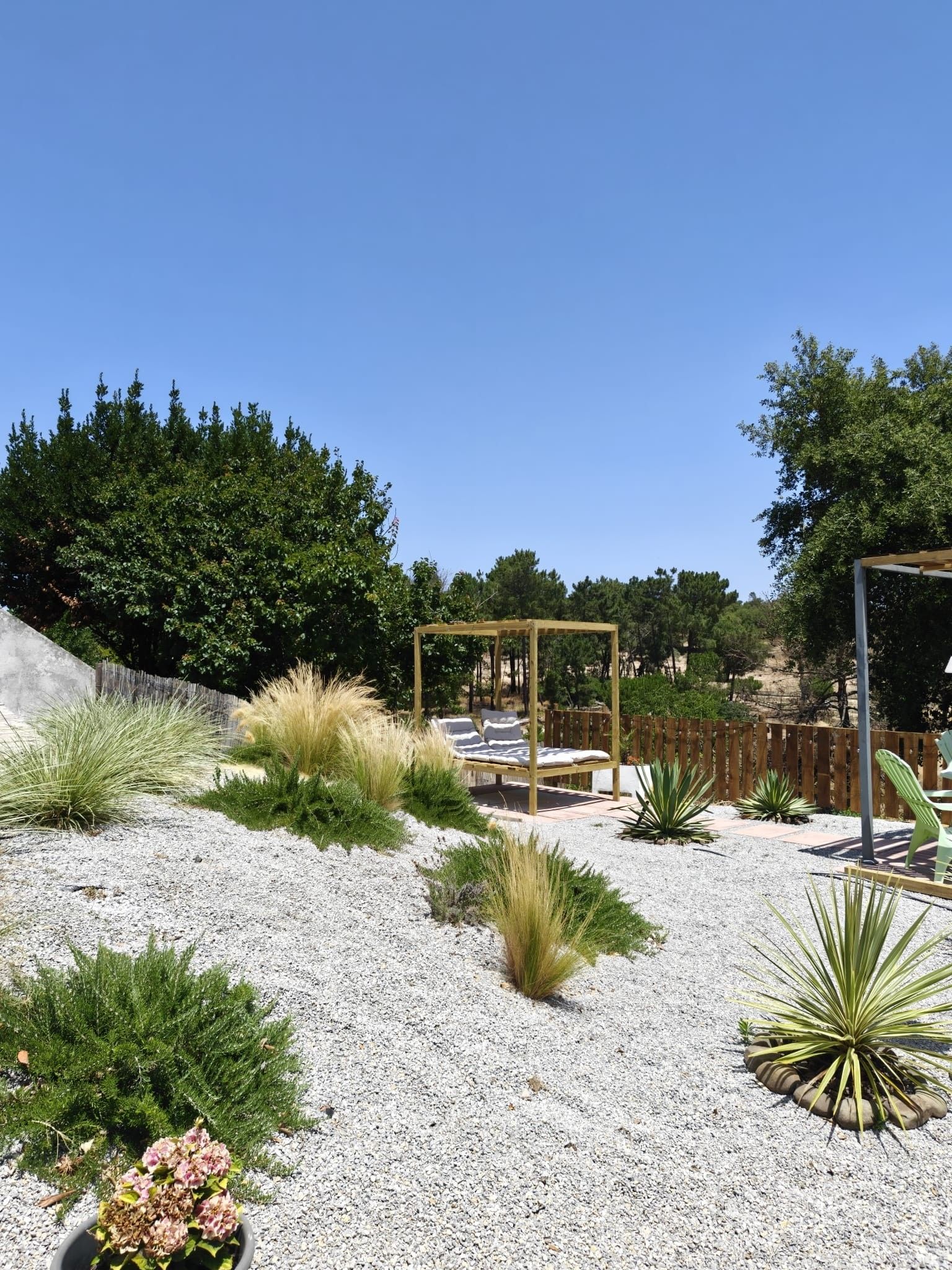 Un jardin agrémenté d’une pergola en bois, d’un sol en gravier et de diverses plantes.