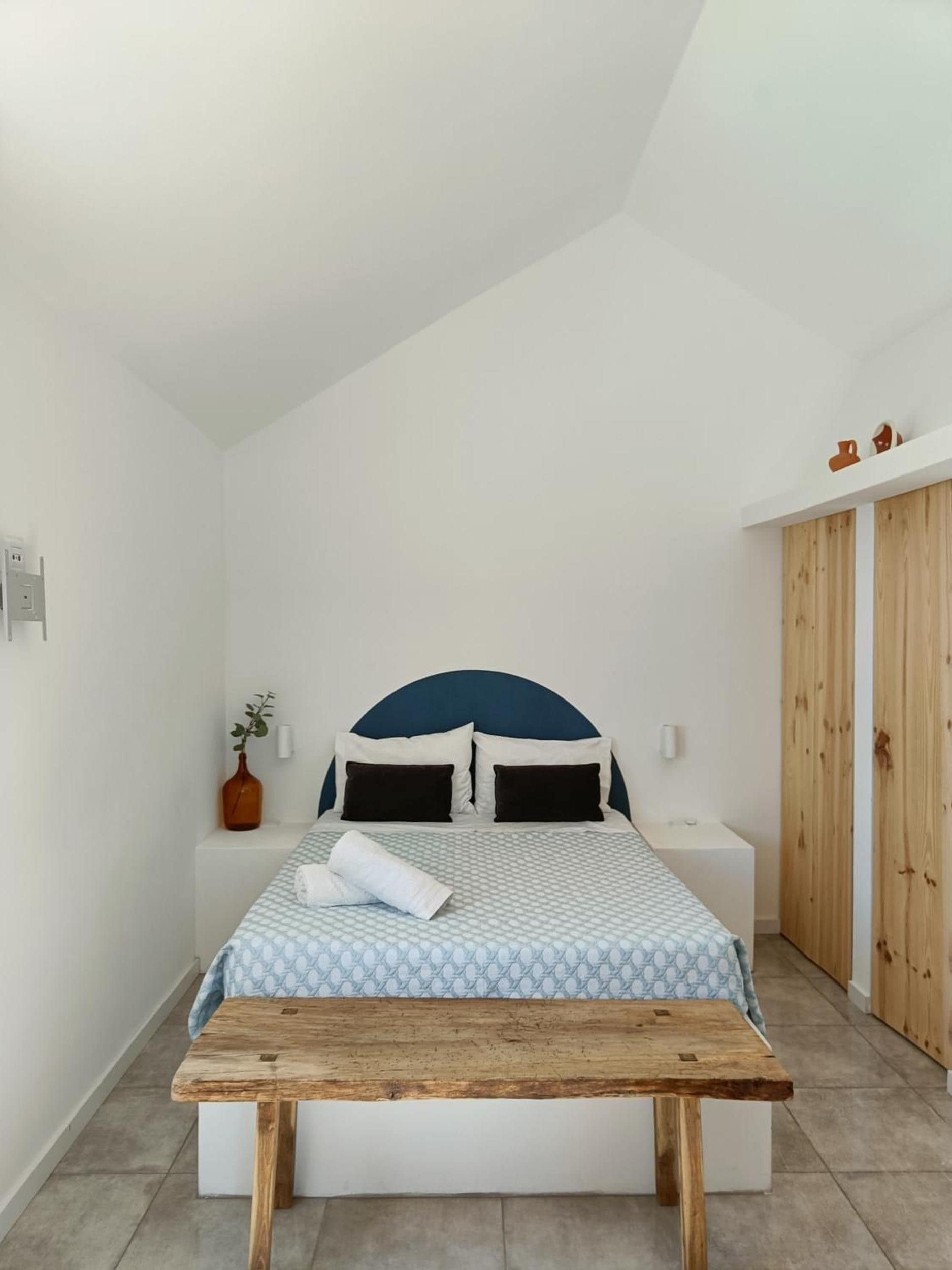 A bedroom with a bed, bedside tables, a wooden bench, a vase with a plant, and a wardrobe.