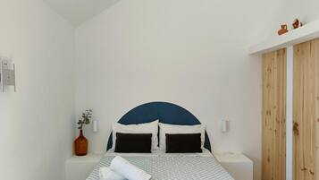 A bedroom with a bed, bedside tables, a wooden bench, a vase with a plant, and a wardrobe.