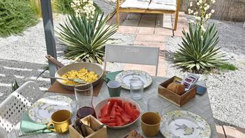 An outdoor dining area with a table set for breakfast, including bread, pastries, and fruit.