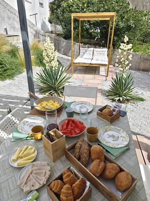 An outdoor dining area with a table set for breakfast, including bread, pastries, and fruit. - Apartment 'Casinha De Lume' with Mountain View, Wi-Fi and Air Conditioning (Melides)