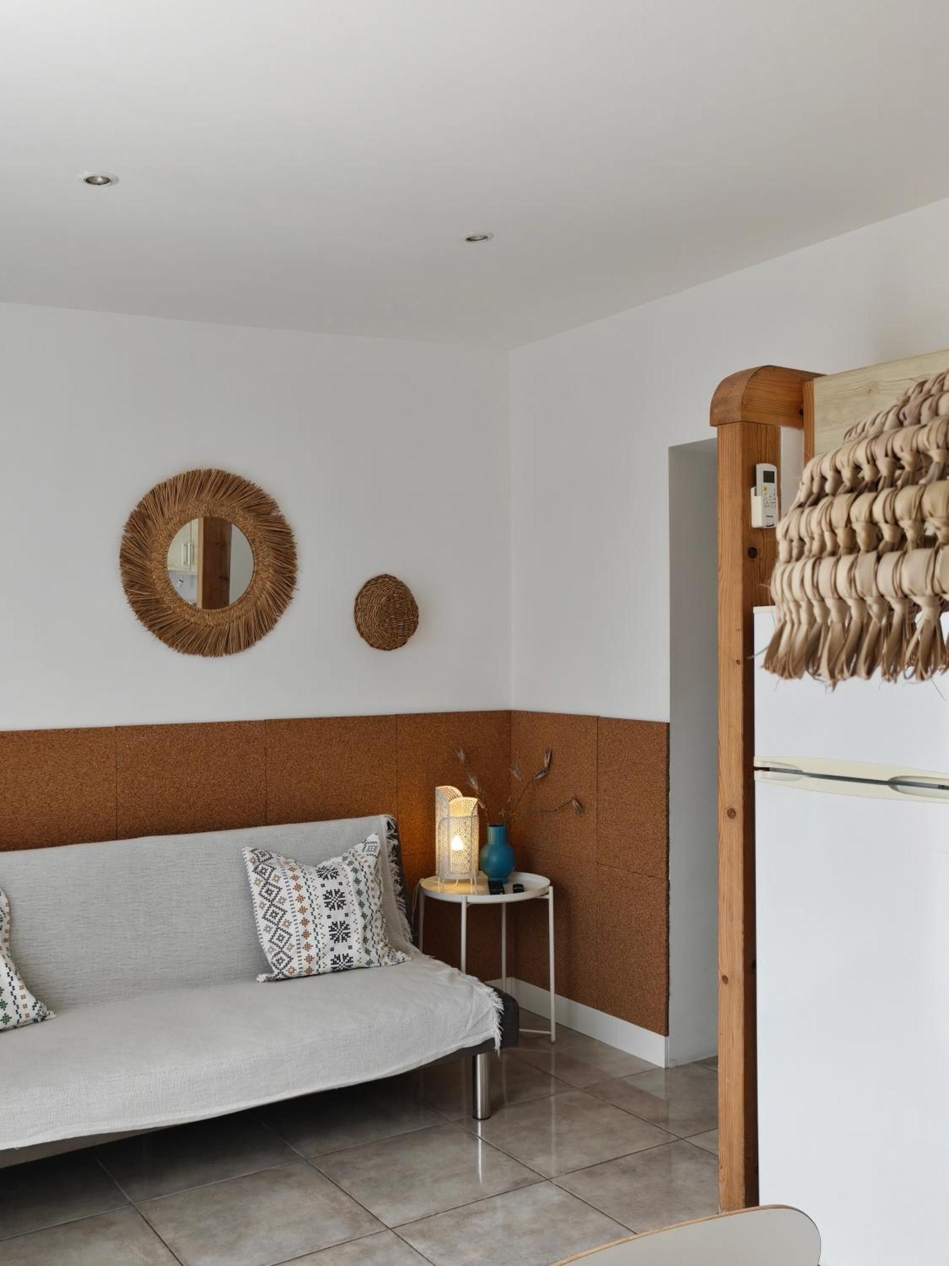 A modern living room with a sofa, two wall-mounted mirrors, a small side table with a lamp, and a wooden structure.