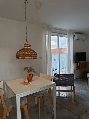 A dining area with a table, chairs, a hanging light fixture, a vase with dried flowers, and a view of the outside through a window with curtains. - Apartment 'Casinha De Lume' with Mountain View, Wi-Fi and Air Conditioning (Melides)