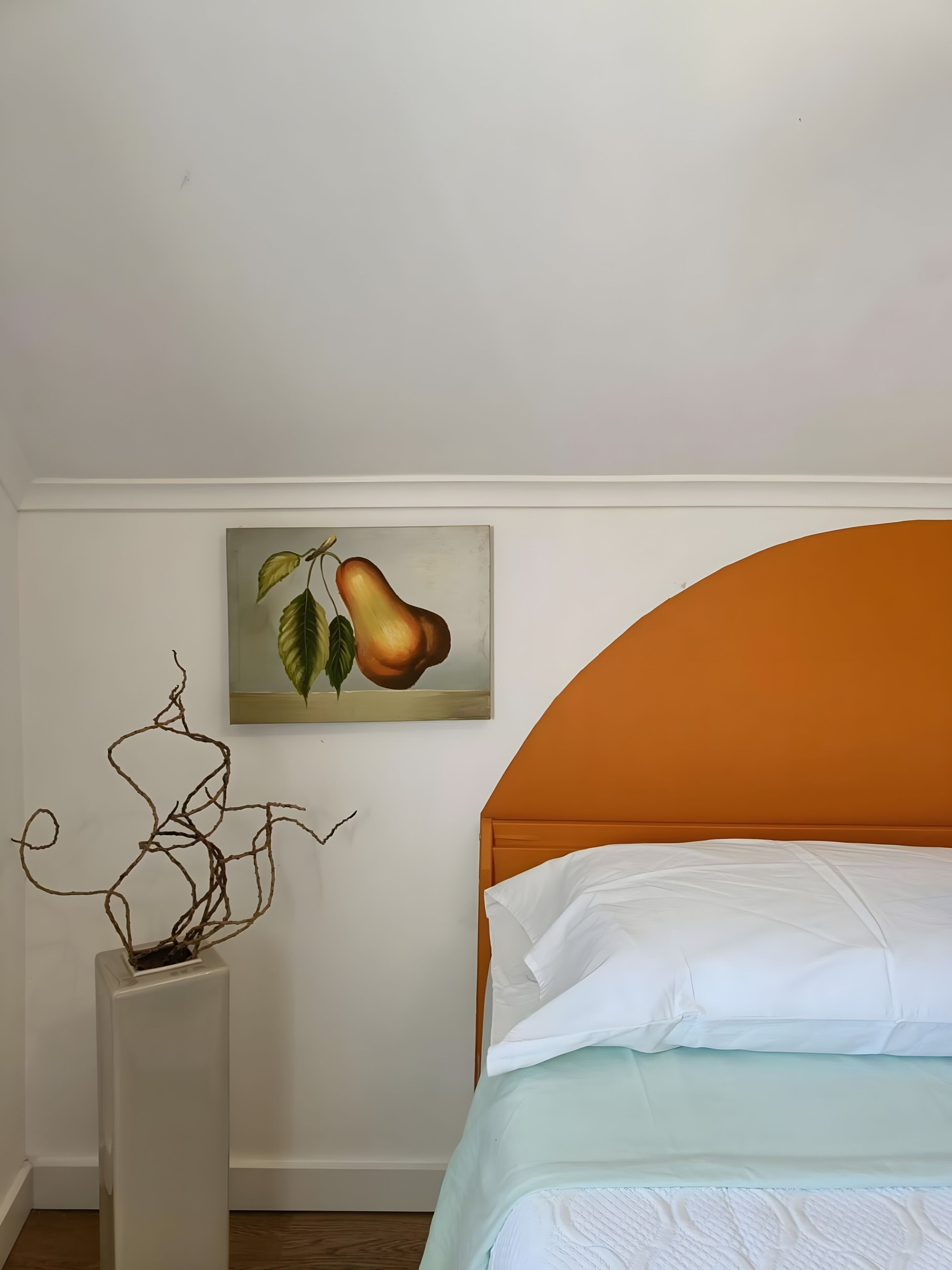 Une chambre à coucher avec un lit, une nature morte représentant des fruits et un vase avec des branches.