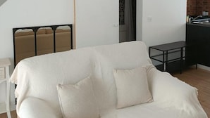 A modern living room with a white sofa, a dining table, and a kitchen area visible through an open door. - Apartment 'Loft Vale De Mouro' with Mountain View, Wi-Fi and Air Conditioning (Melides)