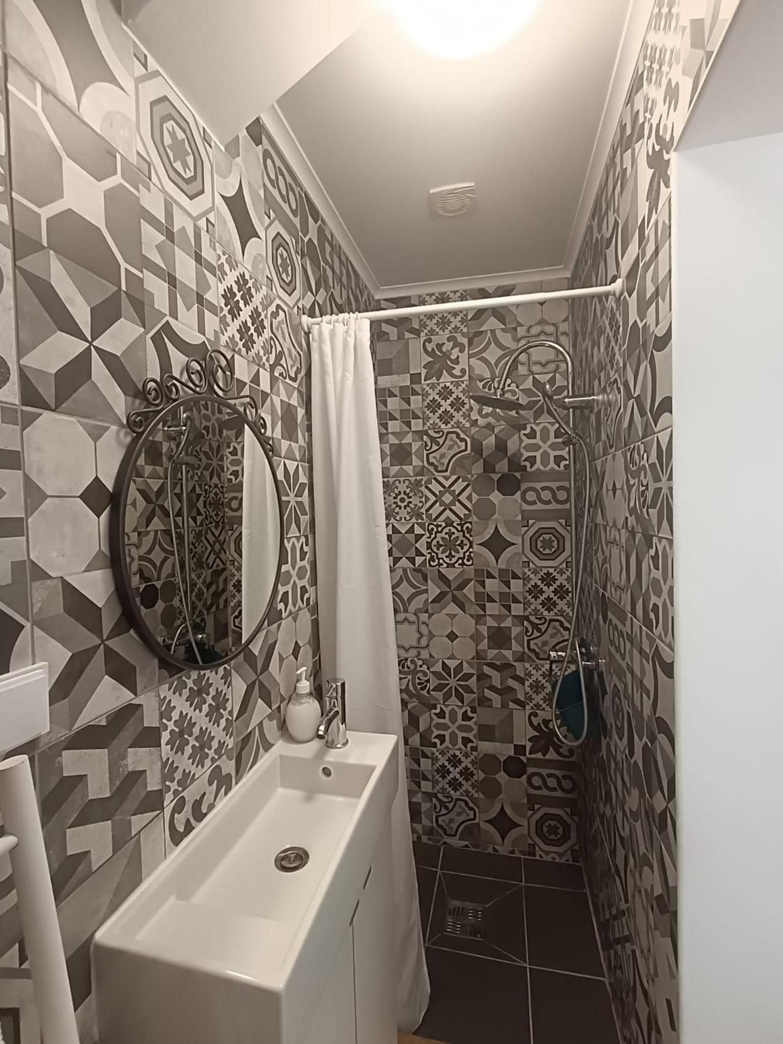 A bathroom with a white sink, a mirror, and a shower area with patterned tiles.
