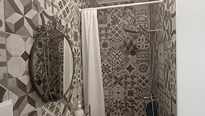 A bathroom with a white sink, a mirror, and a shower area with patterned tiles. - Apartment 'Loft Vale De Mouro' with Mountain View, Wi-Fi and Air Conditioning (Melides)