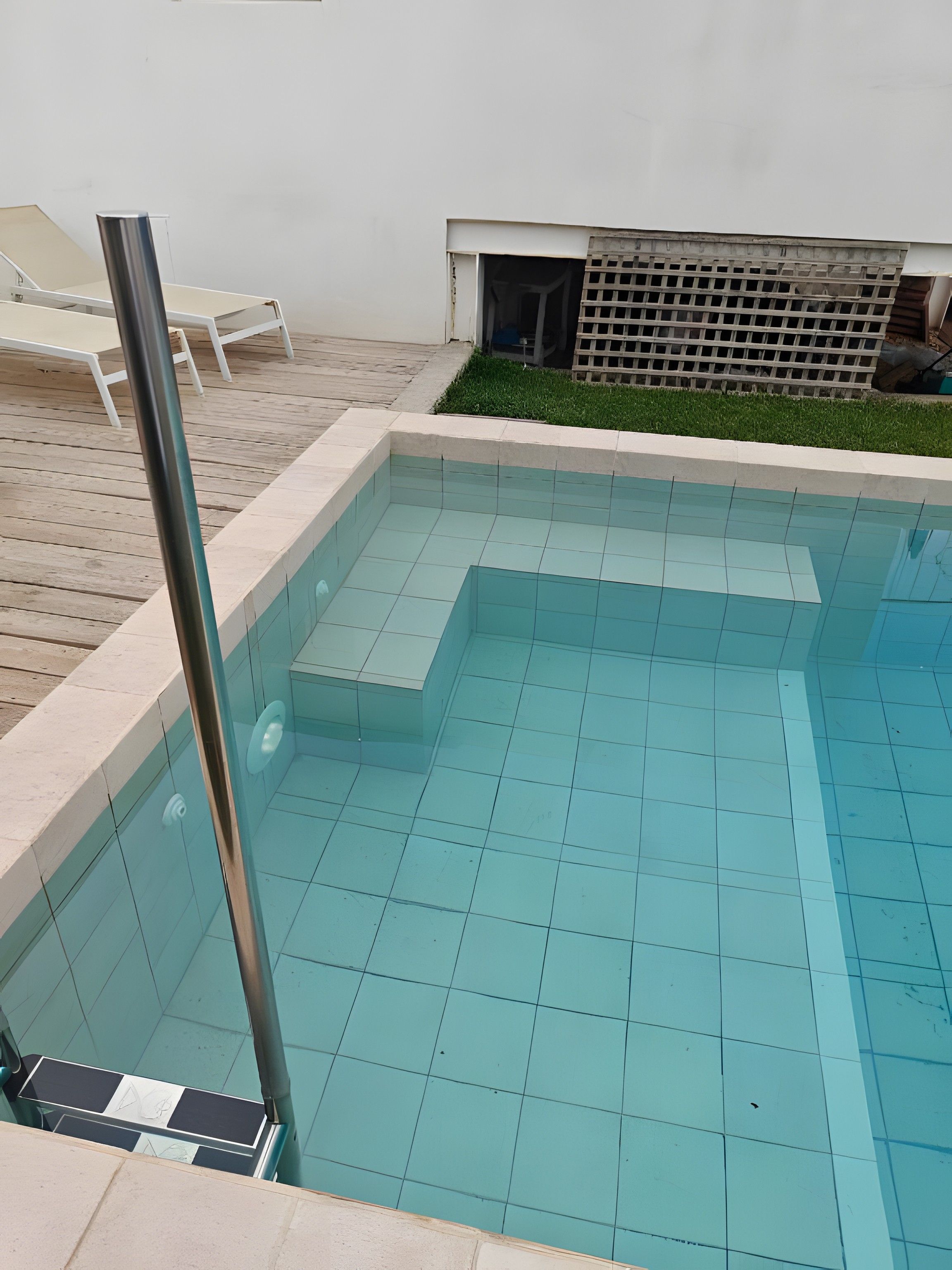 Une piscine avec une terrasse carrelée et un poteau en métal.