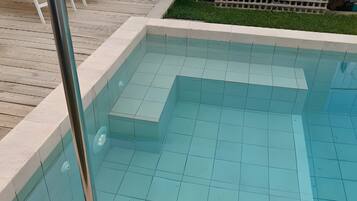 Une piscine avec une terrasse carrelée et un poteau en métal.