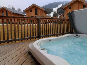 A wooden deck with a hot tub, surrounded by wooden cabins with a mountainous backdrop. - One-bedroom Cabin (Sankt Georgen am Kreischberg)