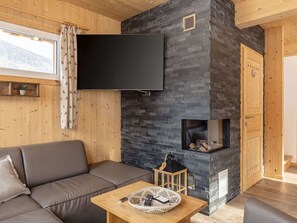 A cozy living room with a stone fireplace, a flat-screen TV, a sofa, and a small table with a basket. - One-bedroom Cabin (Sankt Georgen am Kreischberg)