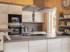 A modern kitchen with built-in appliances, a wooden wall, and a clock. - One-bedroom Cabin (Sankt Georgen am Kreischberg)