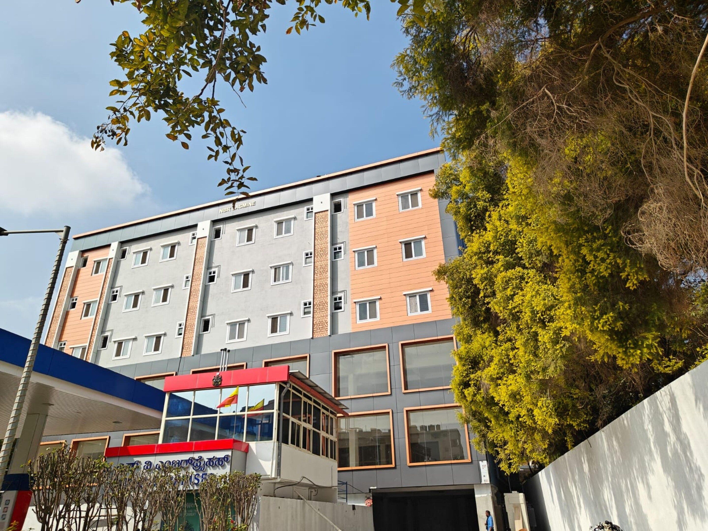 Un edificio de varios pisos con un diseño arquitectónico moderno, que combina fachadas de vidrio y ladrillo, y una entrada destacada con un toldo rojo y blanco.