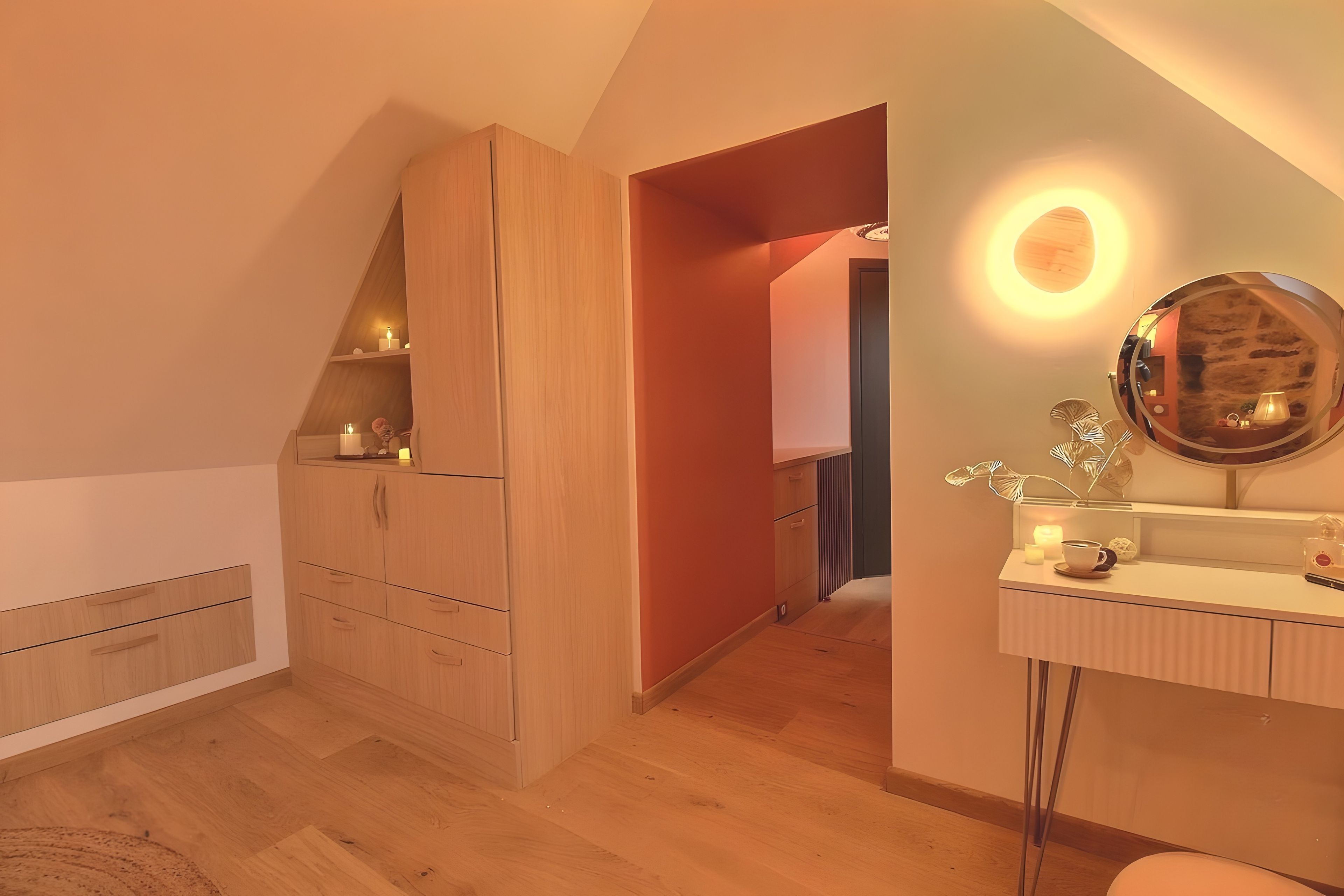 Une chambre avec une armoire en bois, une table de chevet avec un miroir et un petit coin salon avec un coussin.
