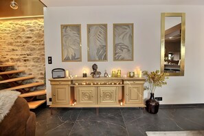 Una sala de estar con pared de piedra, una escalera de madera, una consola de color crema con luces decorativas y un espejo grande.