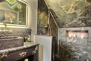 Une salle de bain moderne avec un mur en marbre, une douche et un meuble-lavabo doté d’un évier et d’un miroir.