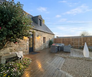 Una casa de piedra con una terraza de madera, un muro de piedra y una cerca de madera.
