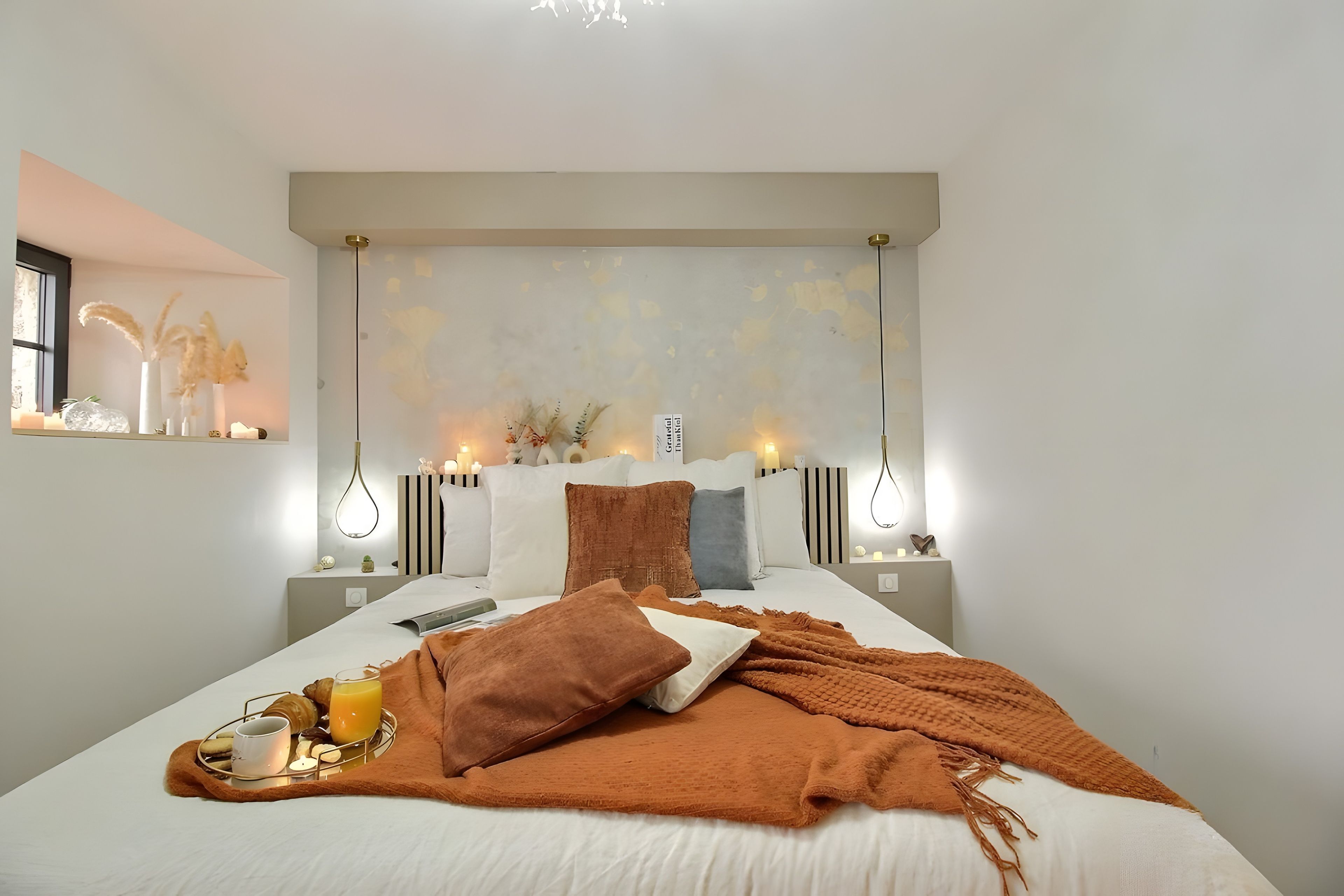 A hotel room with a large bed, bedside tables, a nightstand, a window, and a wall-mounted light fixture.