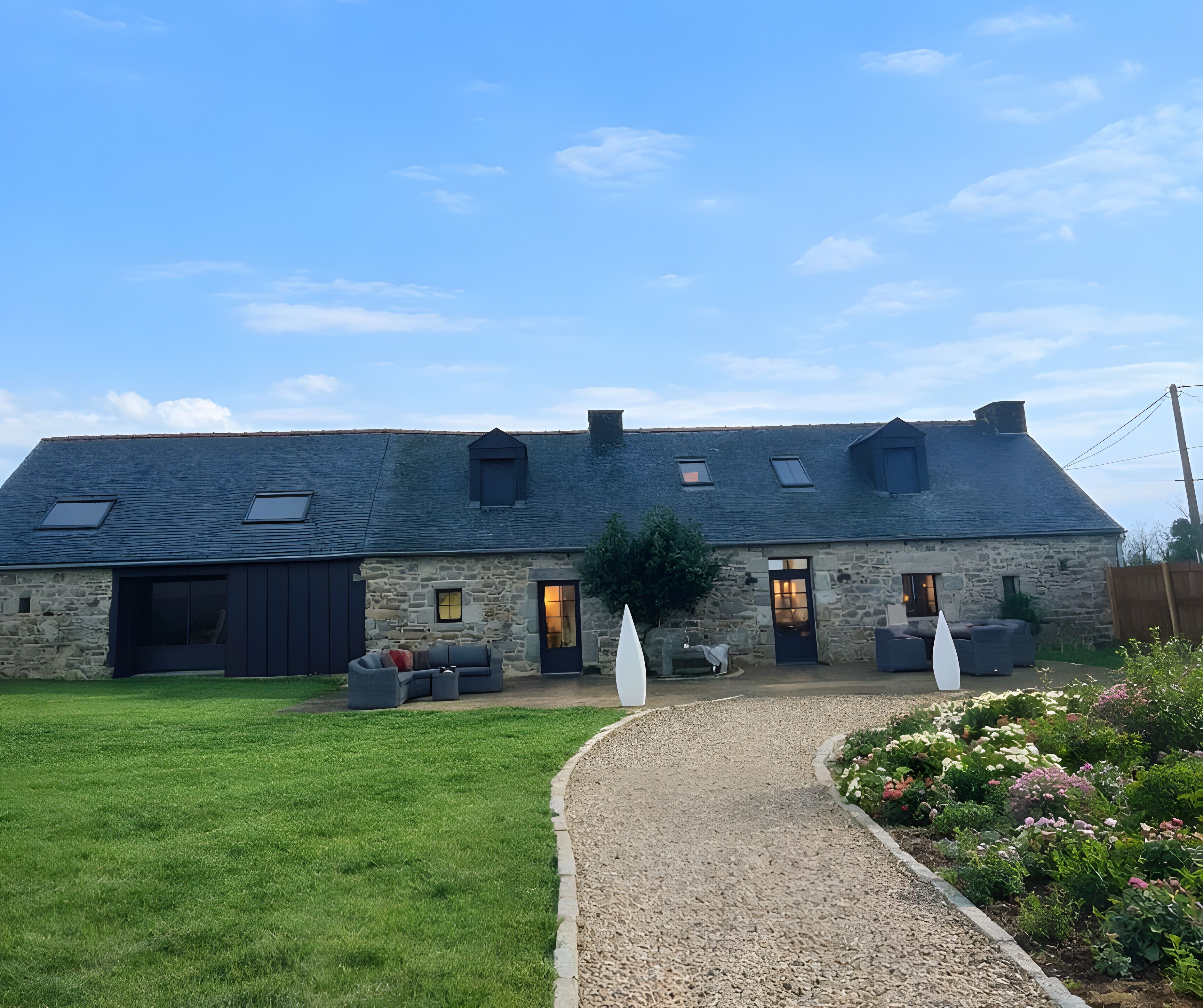 Un bâtiment en pierre avec un toit en pente, une allée gravillonnée et une pelouse verdoyante.