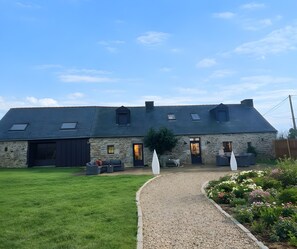 Un bâtiment en pierre avec un toit en pente, une allée gravillonnée et une pelouse verdoyante.