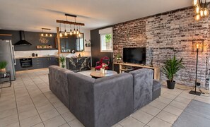 A modern living room with a grey sectional sofa, a flat-screen TV, and a brick wall.